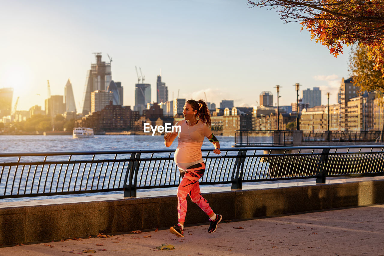 Pregnant woman running on promenade in city during sunset