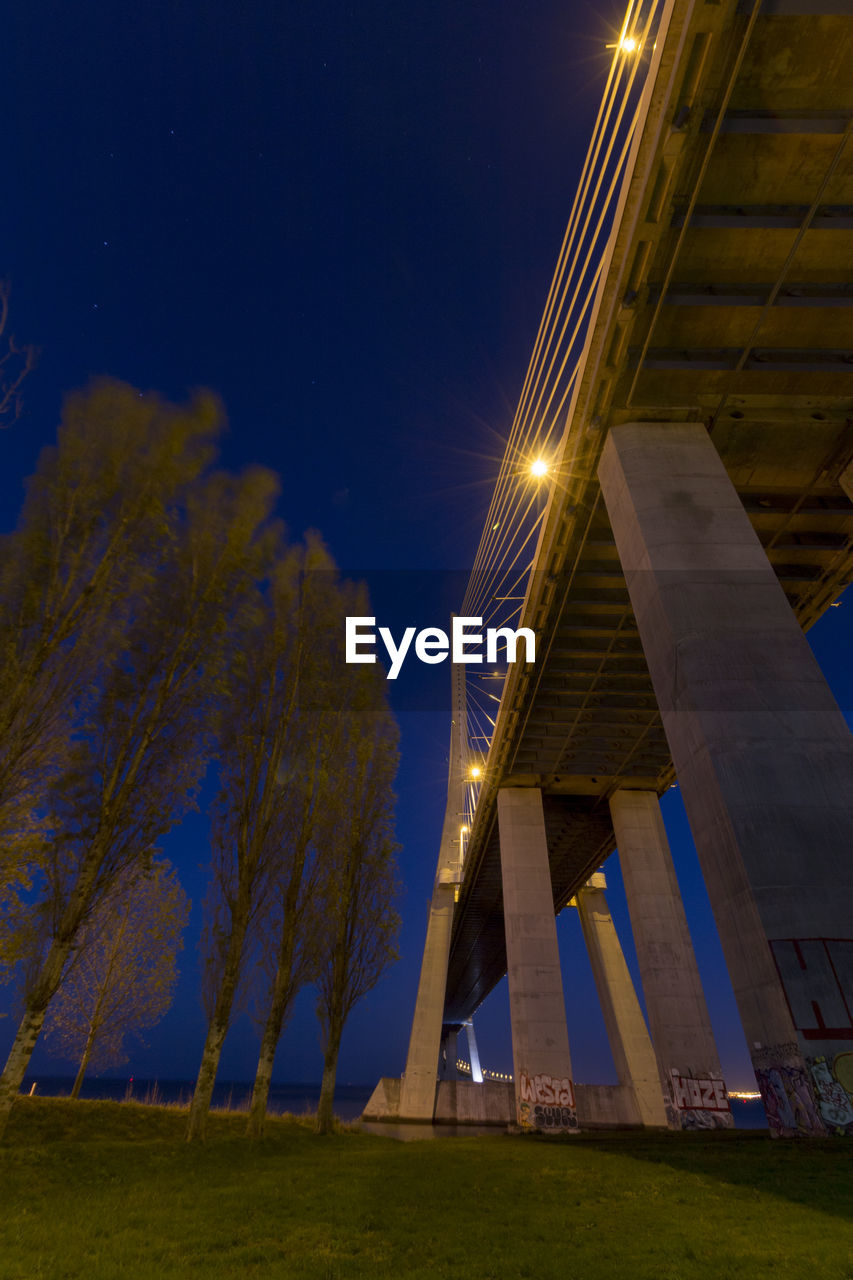 Low angle view of bridge by trees on field