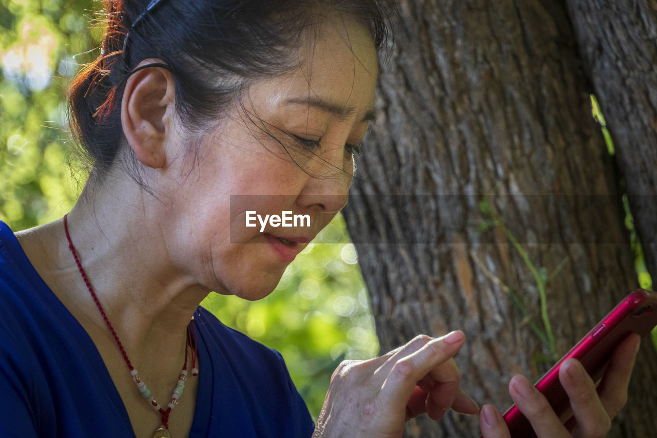 PORTRAIT OF WOMAN HOLDING TREE TRUNK AGAINST PLANTS