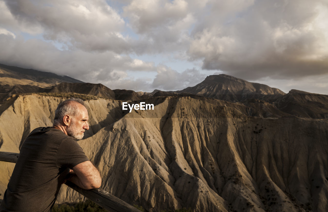 Side view of adult man looking at view in tabernas desert in almeria, spain, against cloudy sky