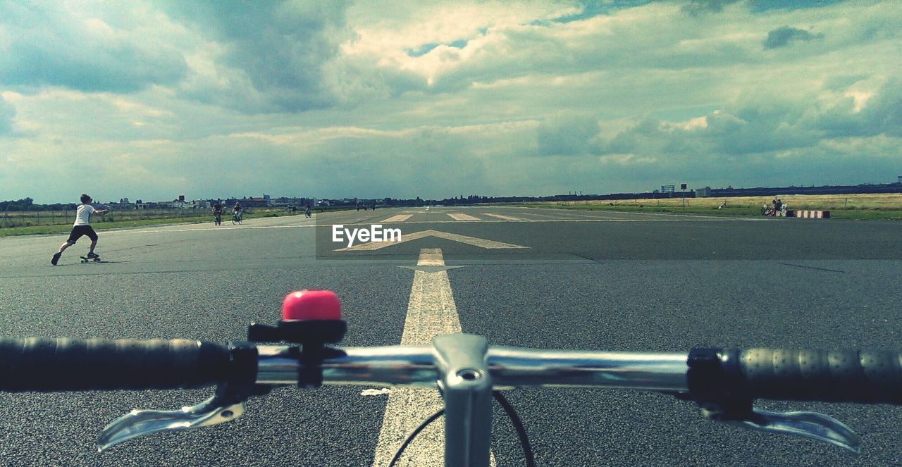 Cropped image of bicycle on airport runway against cloudy sky