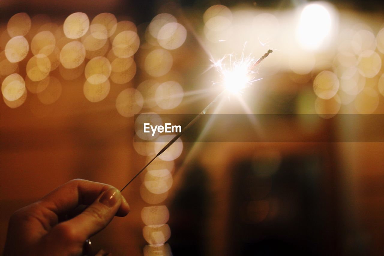 Cropped hand holding illuminated sparkler at night