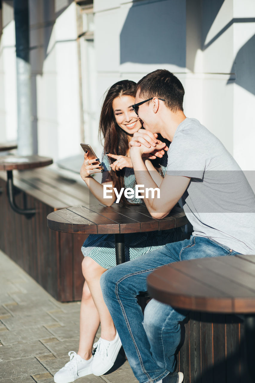 YOUNG COUPLE SITTING ON WOMAN HOLDING CAMERA