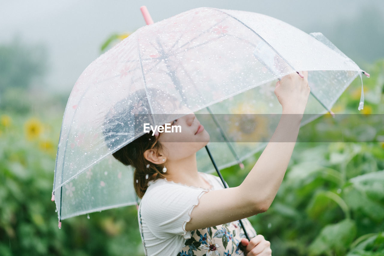 Young woman holding transparent umbrella on rainy day