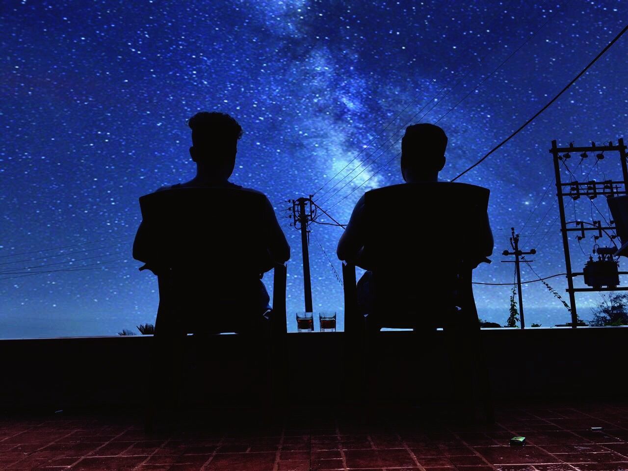 Silhouette men sitting against sky at night