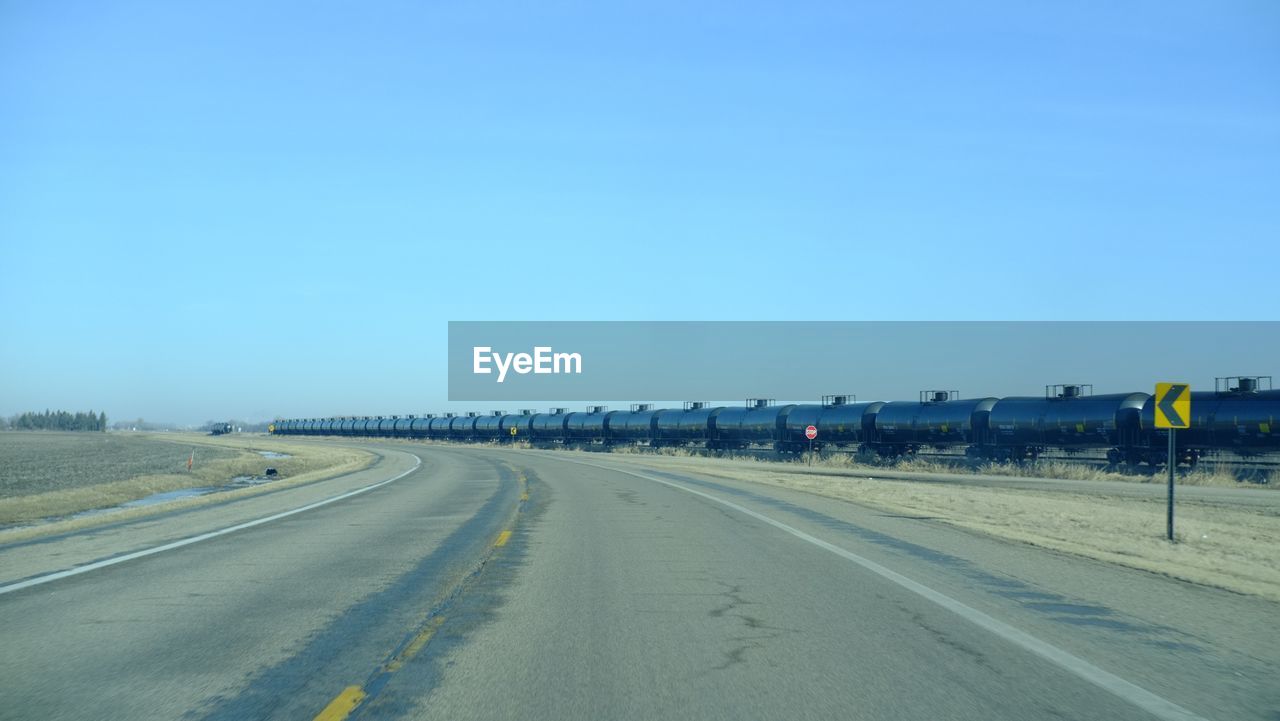 Empty road by freight train against clear sky
