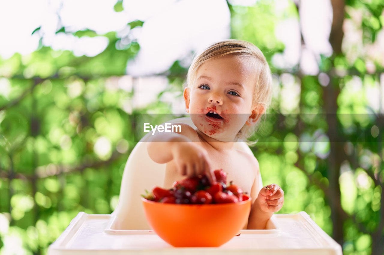 Baby girl sitting while eating strawberry at home