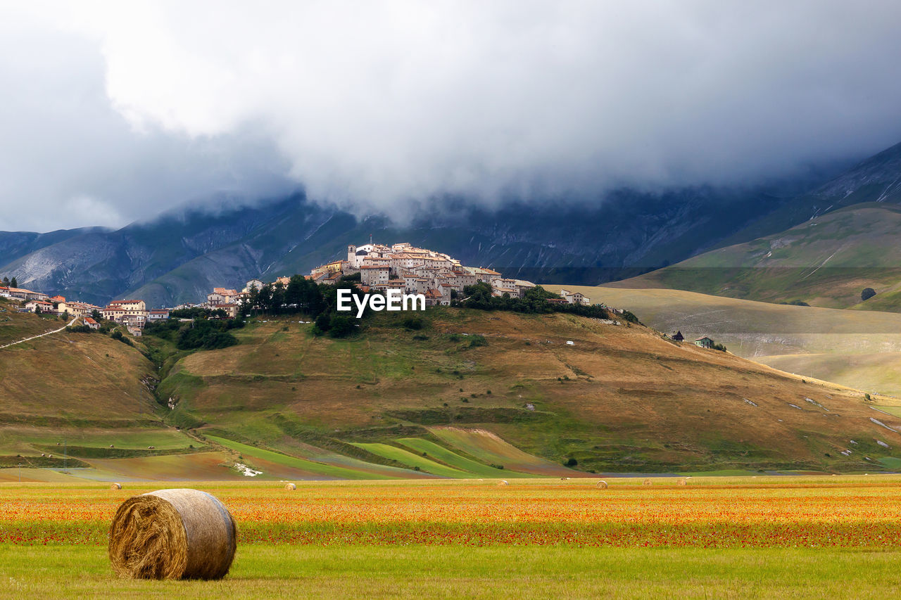 Hay bale on farm by mountains against cloudy sky