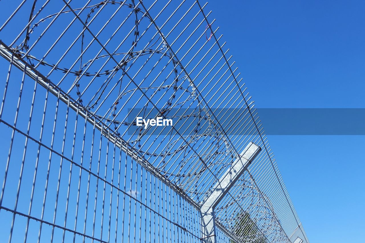 LOW ANGLE VIEW OF METALLIC FENCE AGAINST CLEAR BLUE SKY