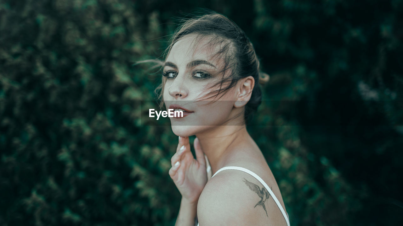 Portrait of young woman looking away against plants