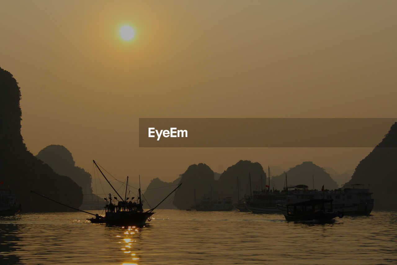 Silhouette boats on halong bay by rock formations against clear sky
