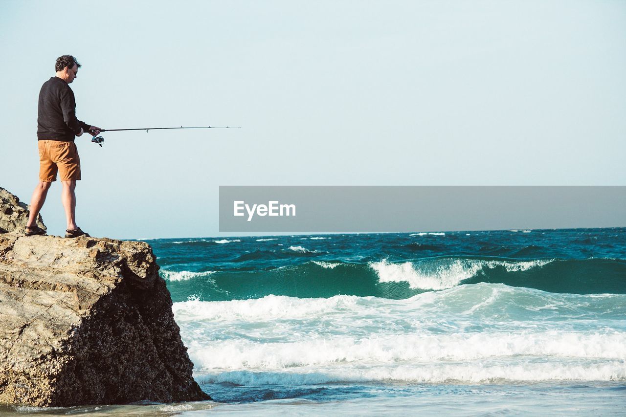 Full length of man fishing at sea against clear sky