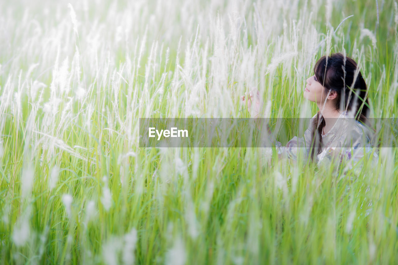 Side view of mid adult woman looking away while sitting amidst plants