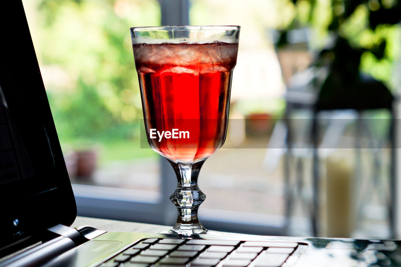 Close-up of red drink in glass by laptop on table 