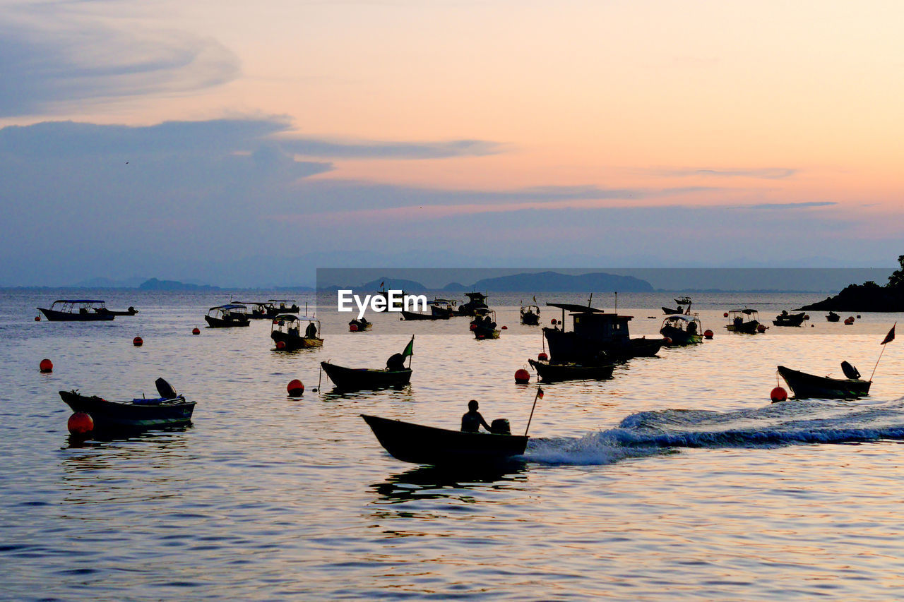 Fishing boats on sea against sky during sunset