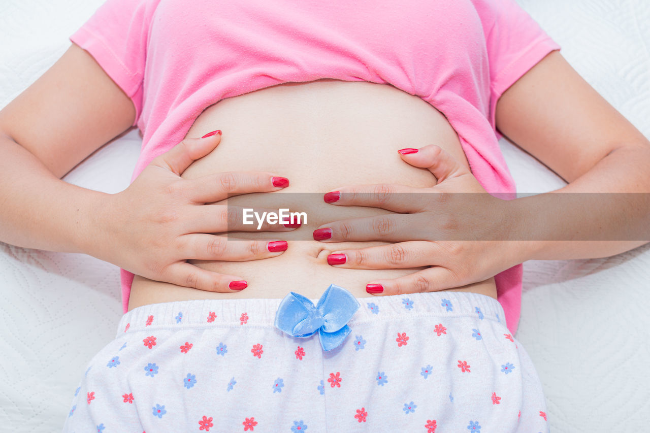 midsection of pregnant woman holding abdomen while lying on bed
