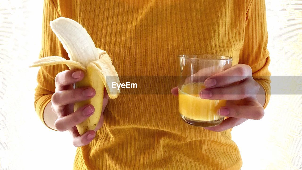 Close-up of woman holding banana and juice against white background