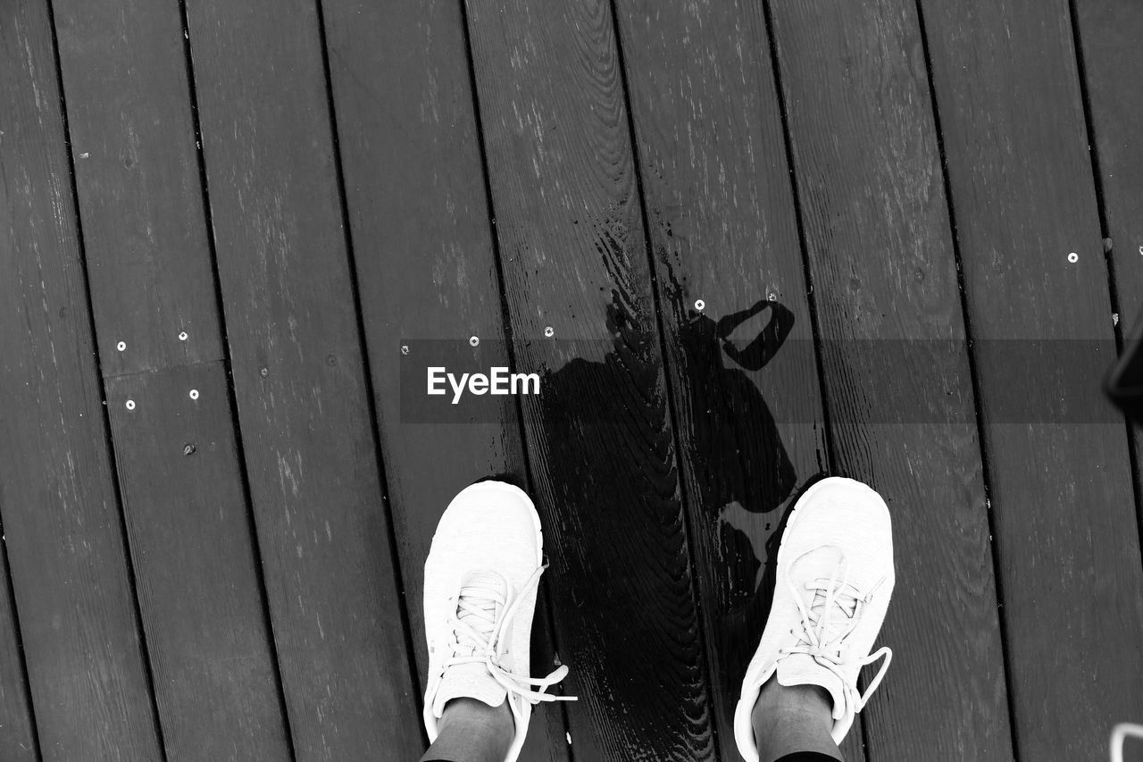 LOW SECTION OF PERSON STANDING ON WOODEN BOARDWALK