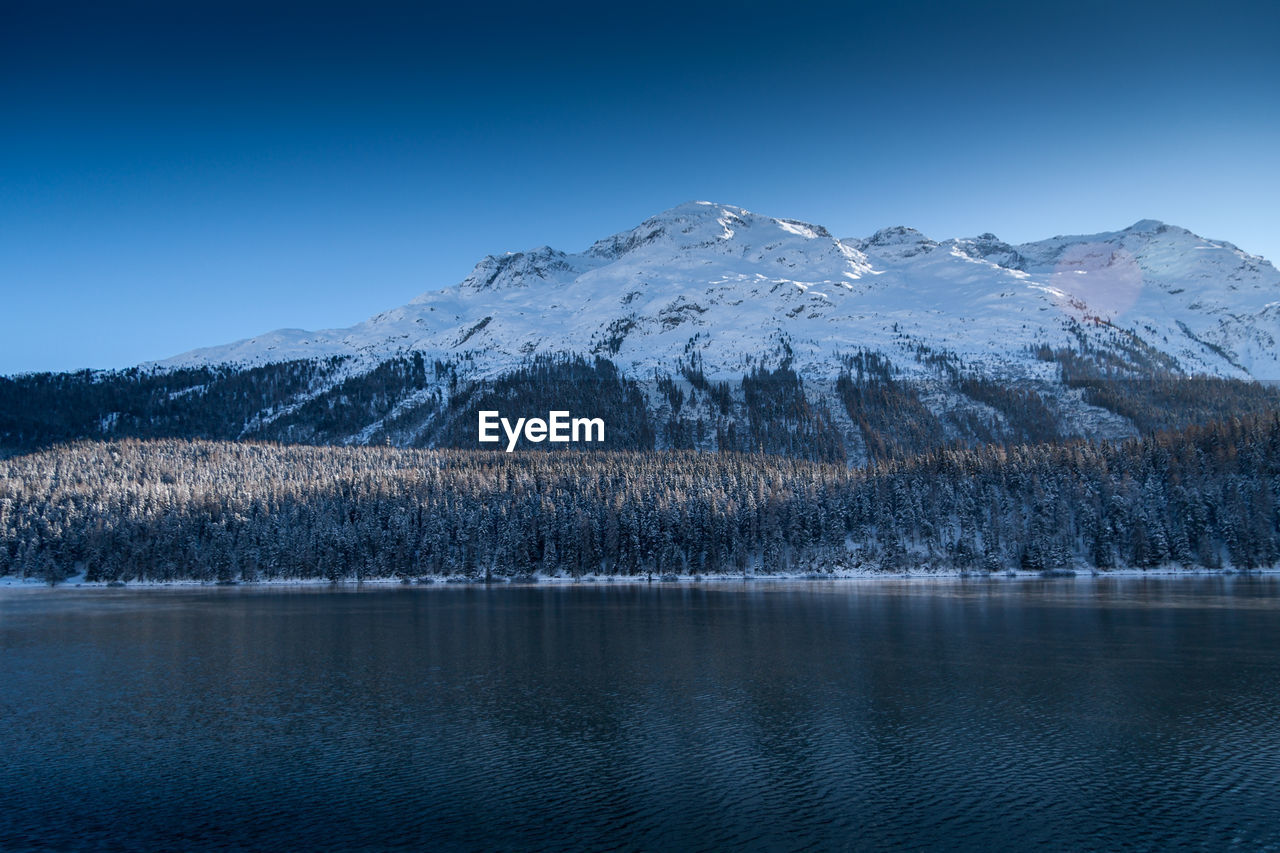 Scenic view of lake and snowcapped mountains against clear blue sky