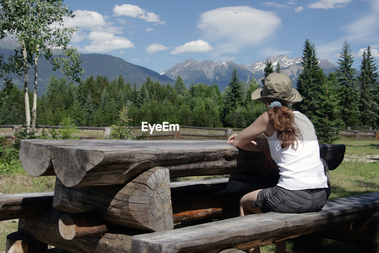 Rear view of woman sitting on wood against mountains