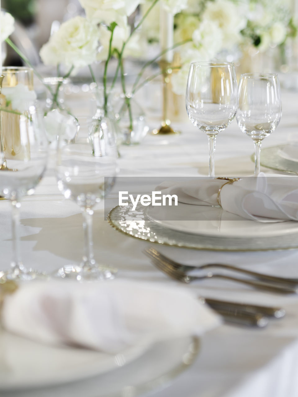 Table serves for banquet. transparent wine glasses, plates and shiny cutlery on white table cloth.