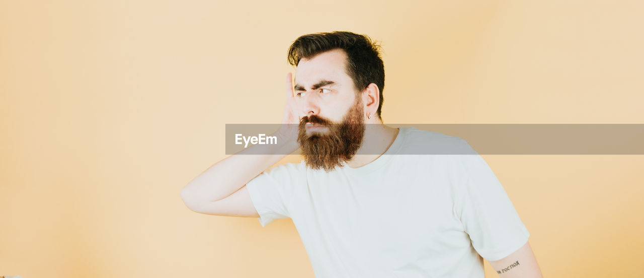 one person, beard, facial hair, adult, indoors, men, studio shot, waist up, portrait, young adult, copy space, colored background, casual clothing, person, standing, looking, brown hair, lifestyles, front view, looking away, t-shirt, contemplation, emotion, clothing, moustache, hairstyle