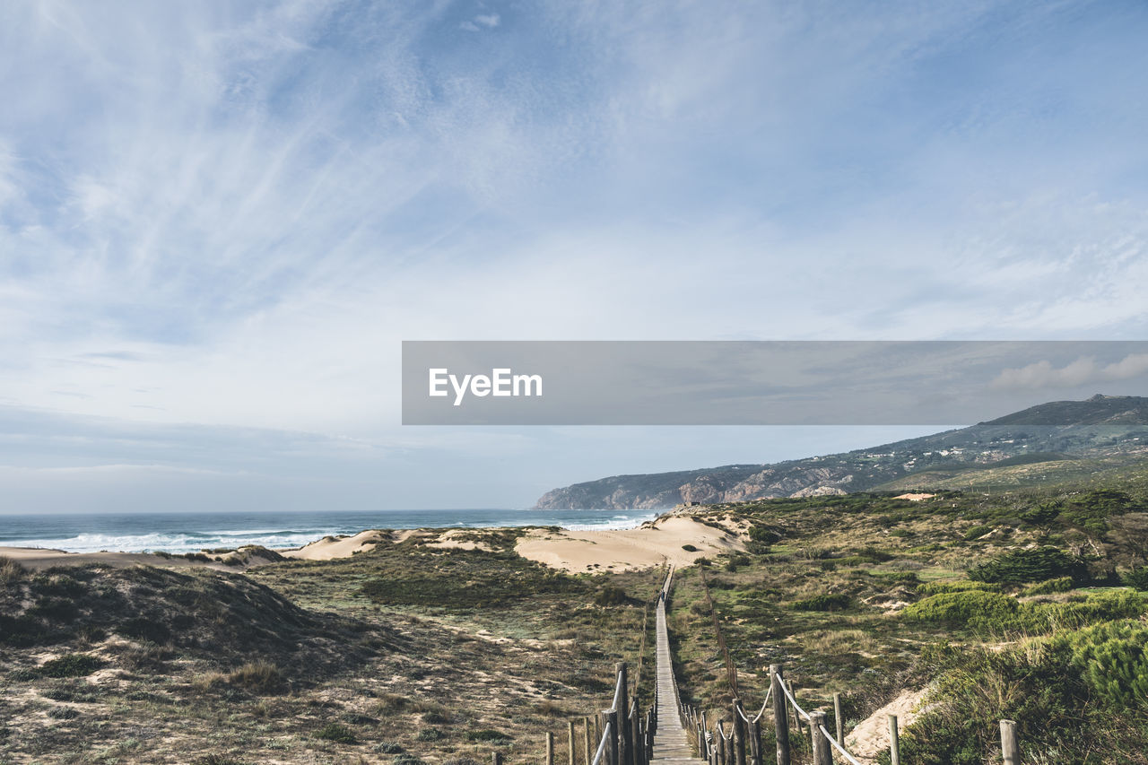 Empty, wooden boardwalk on a beach praia do guincho in sintra. view of grass and sand with hills