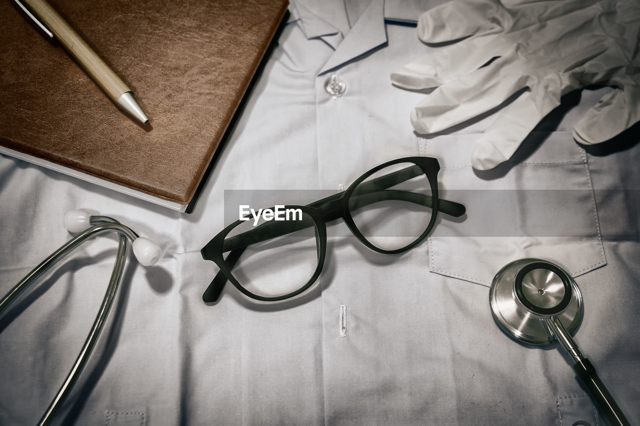 High angle view of eyeglasses with stethoscope by diary and pen on bed