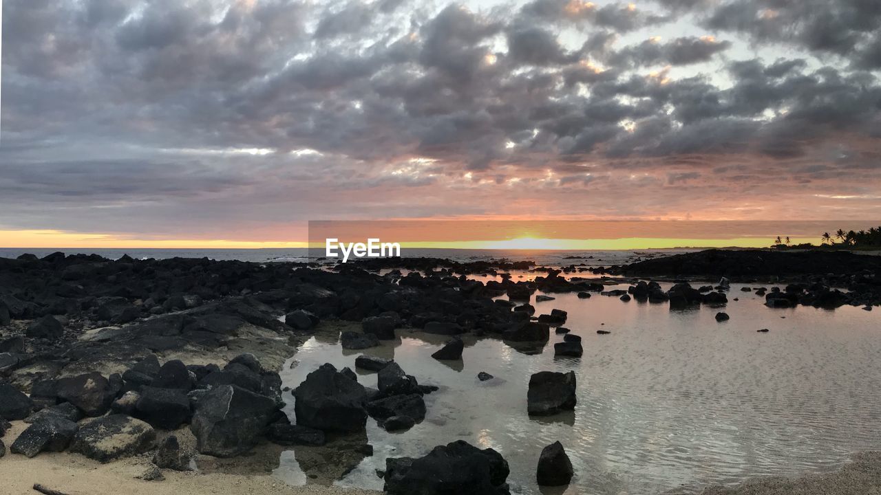 PANORAMIC VIEW OF ROCKS ON SHORE AGAINST SKY DURING SUNSET