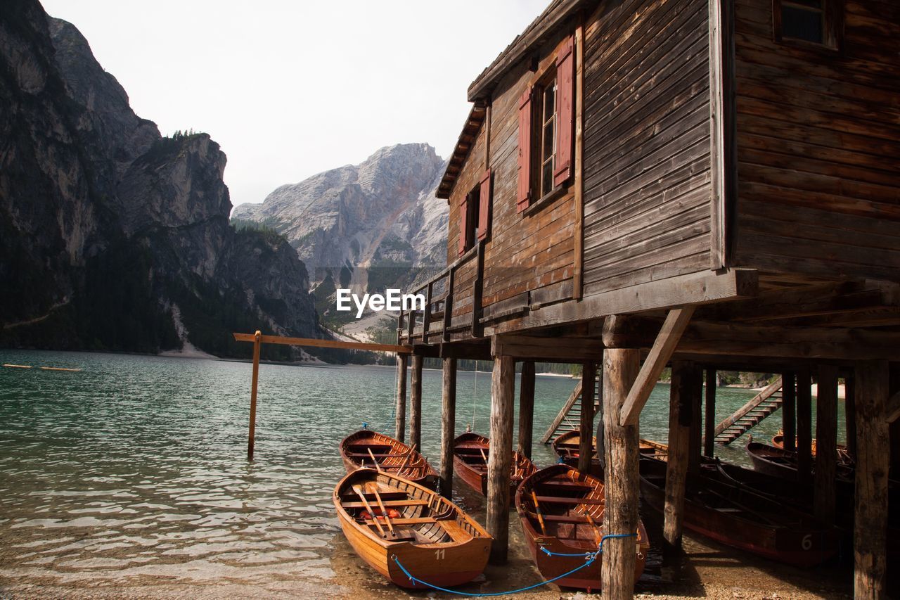 Boats moored below stilt house in lake against mountains