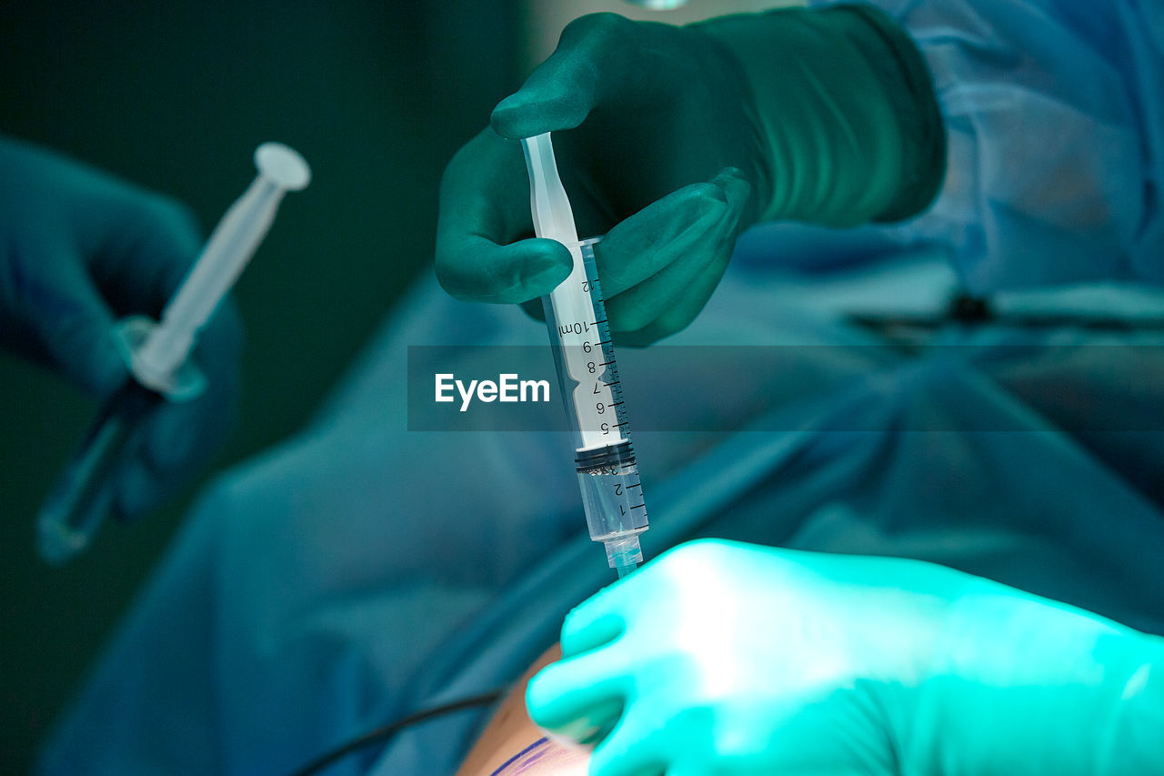 Cropped hands of surgeon giving injection to patient at operating room