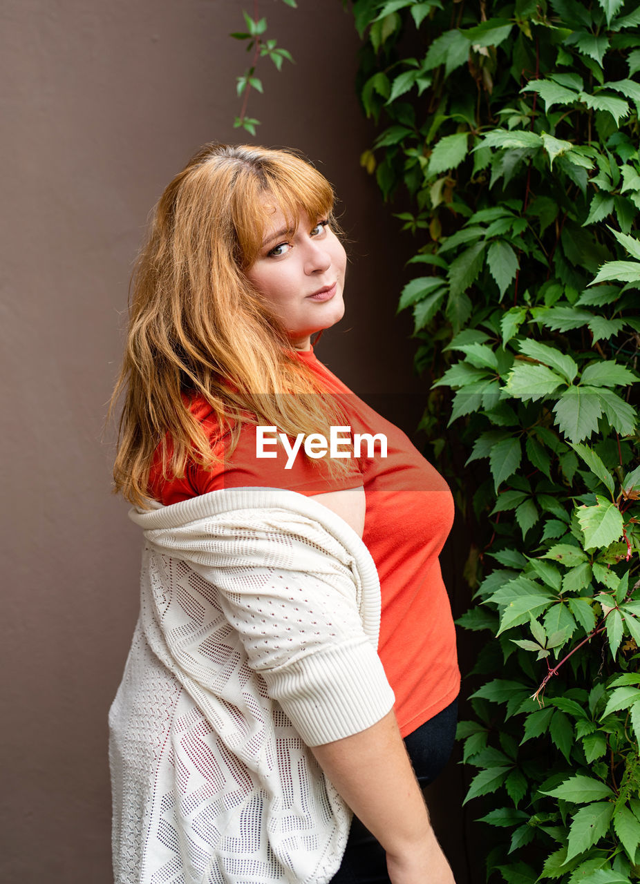 Young woman looking away while standing against plants