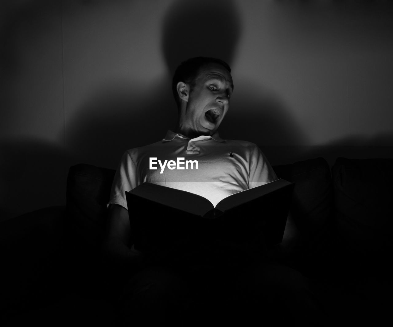 Man making face while reading book in darkroom