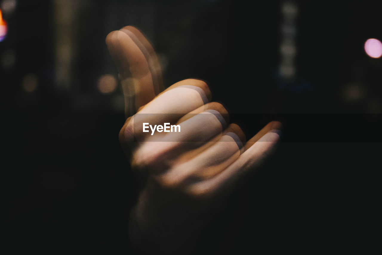Blurred motion of hand gesturing shaka sign in darkroom