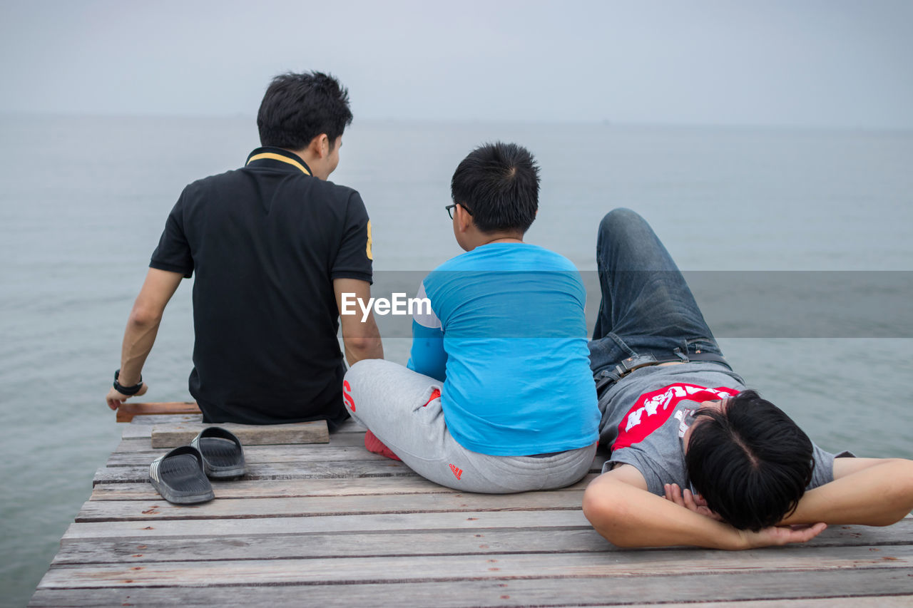 Father with sons relaxing pier by sea against sky
