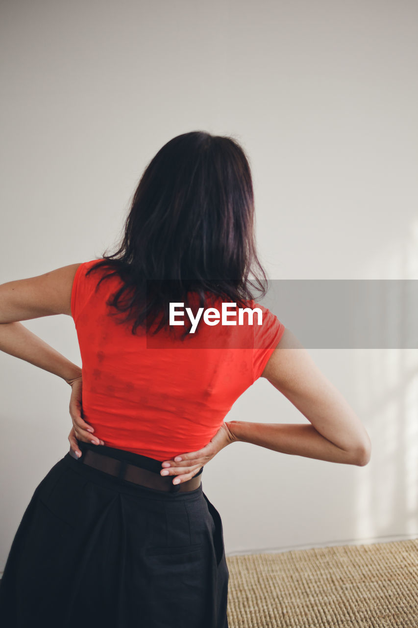 REAR VIEW OF WOMAN STANDING ON WALL AT HOME