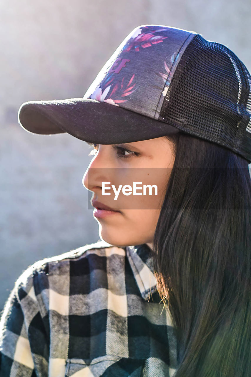 Close-up young woman looking away while wearing cap
