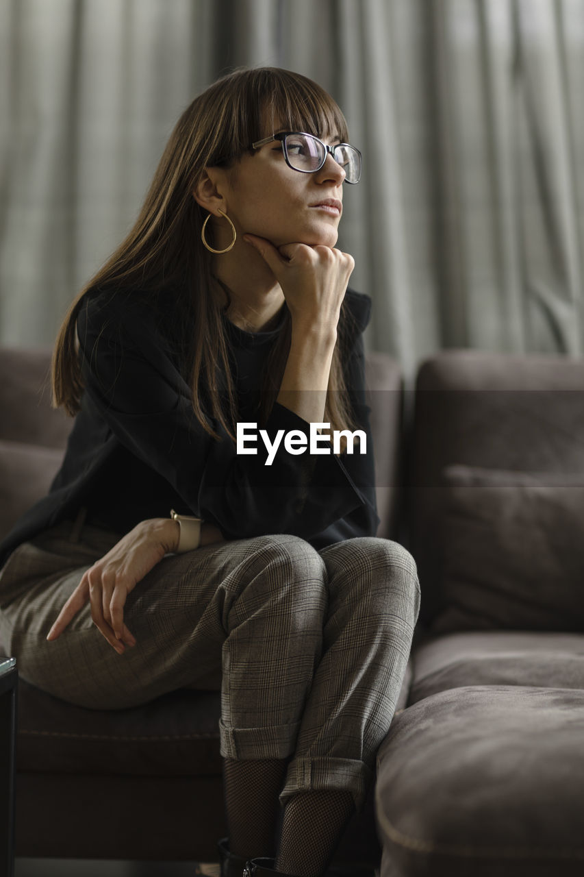 Young woman looking away while sitting on sofa