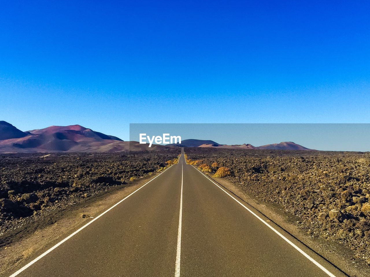 Empty road along landscape against clear blue sky