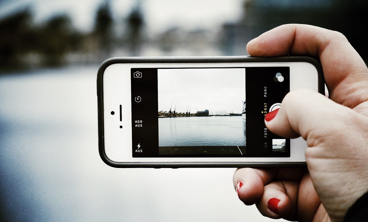 Cropped image of woman hand photographing lake