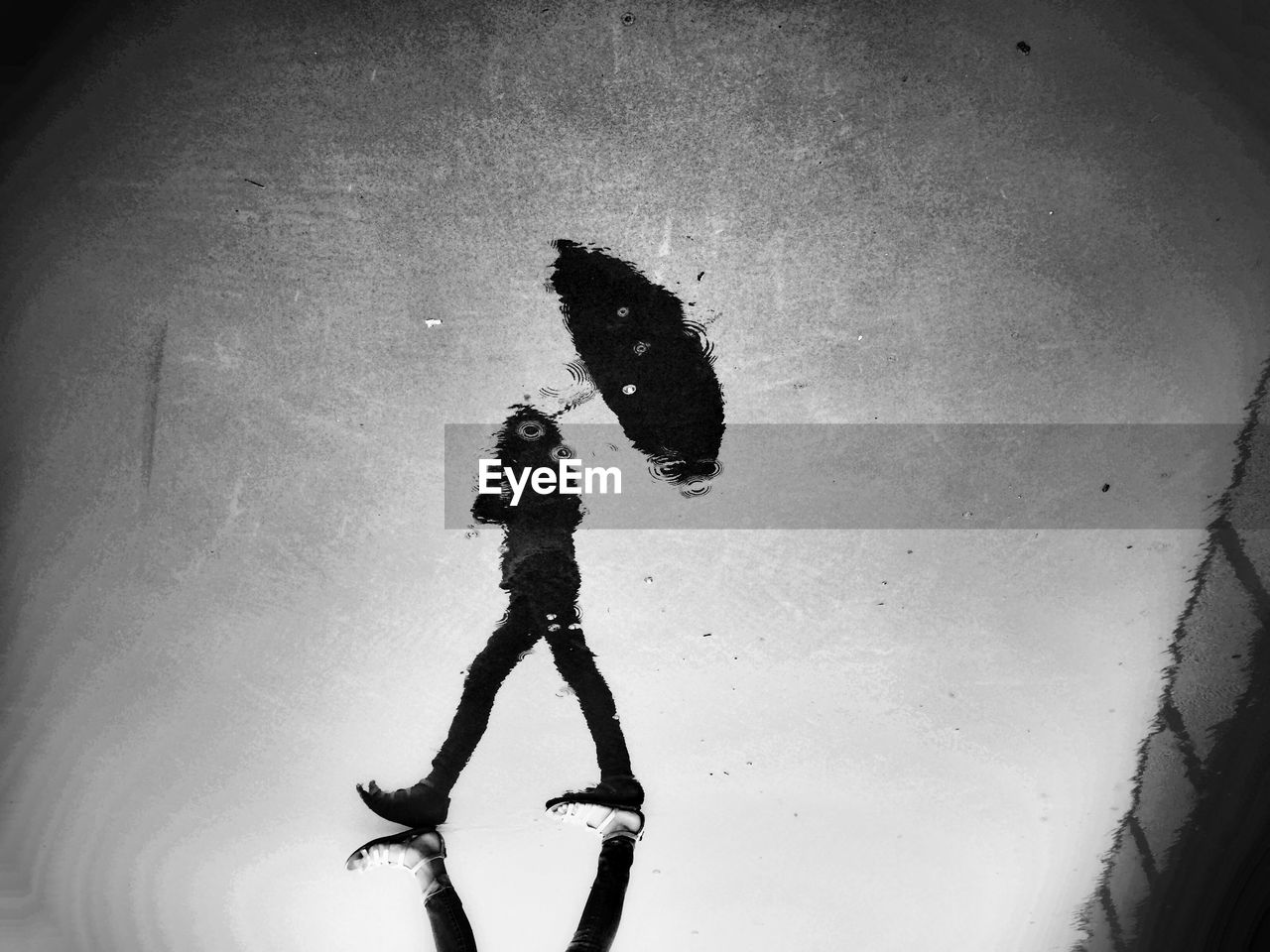 Reflection of person with umbrella on puddle at street