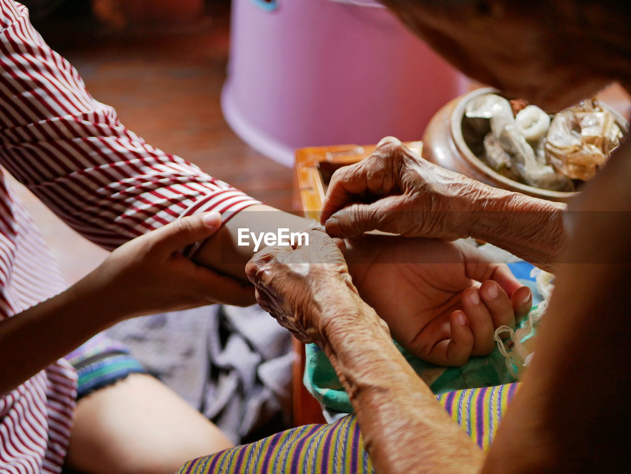 Midsection of senior woman tying string on granddaughter hand