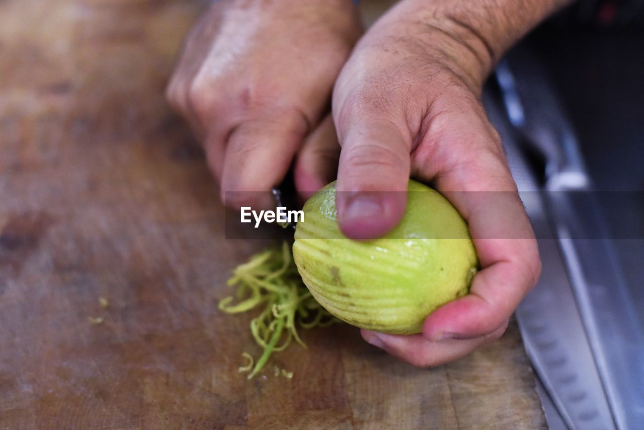 Cropped hand of man peeling lemon on cutting board