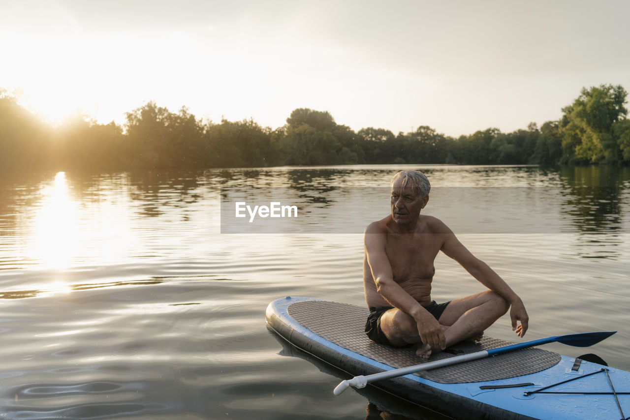 Senior man sitting on sup board at sunset