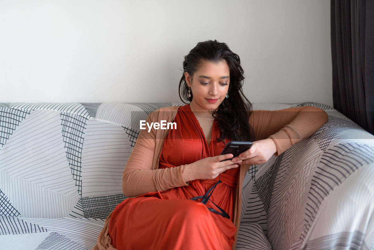 Young woman using phone while sitting on sofa at home