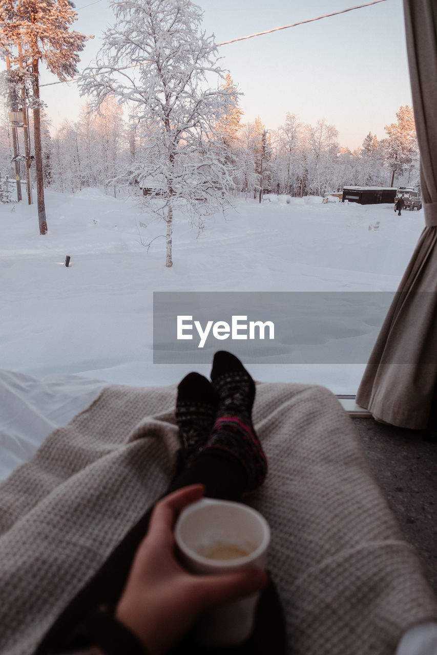 Low section of person with coffee in tent on snow covered trees during winter