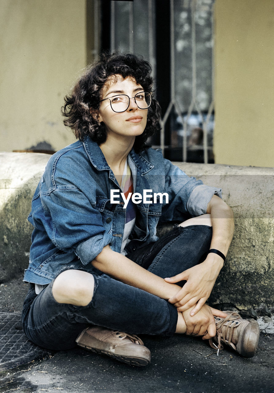 Curly haired woman in glasses sitting on the pavement near the house