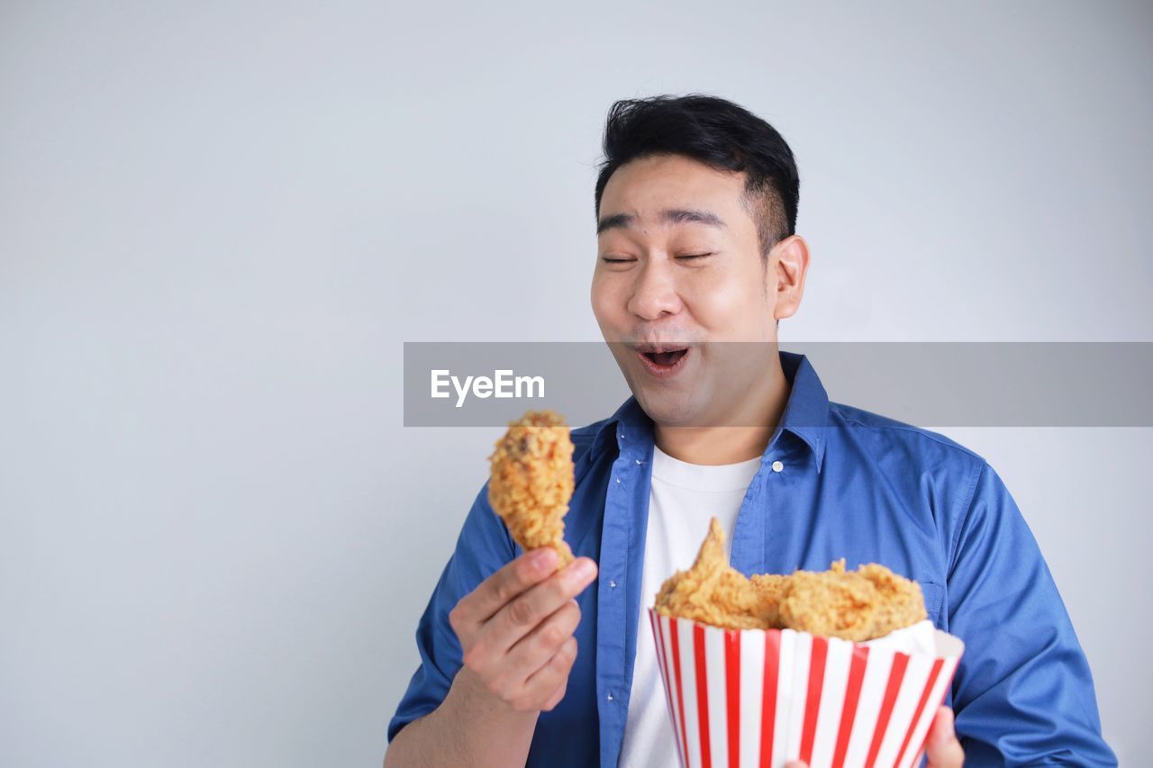 Happy asian man fried chicken bucket and smartphone standing over white background with copy space.