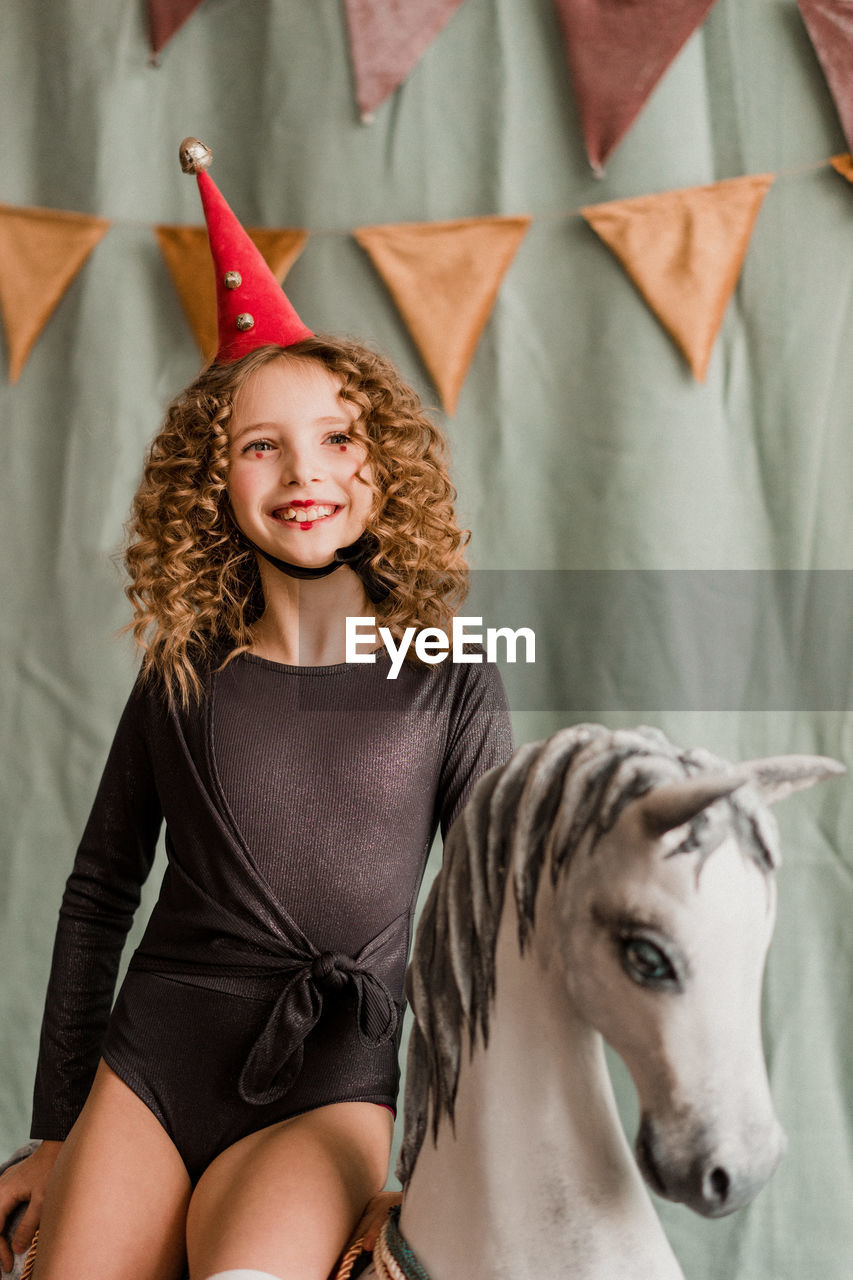 Child girl in circus costume sitting on the carousel horse. halloween