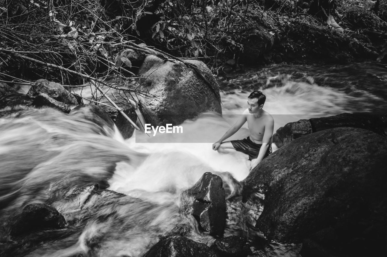 High angle view of shirtless man sitting in river amidst rocks